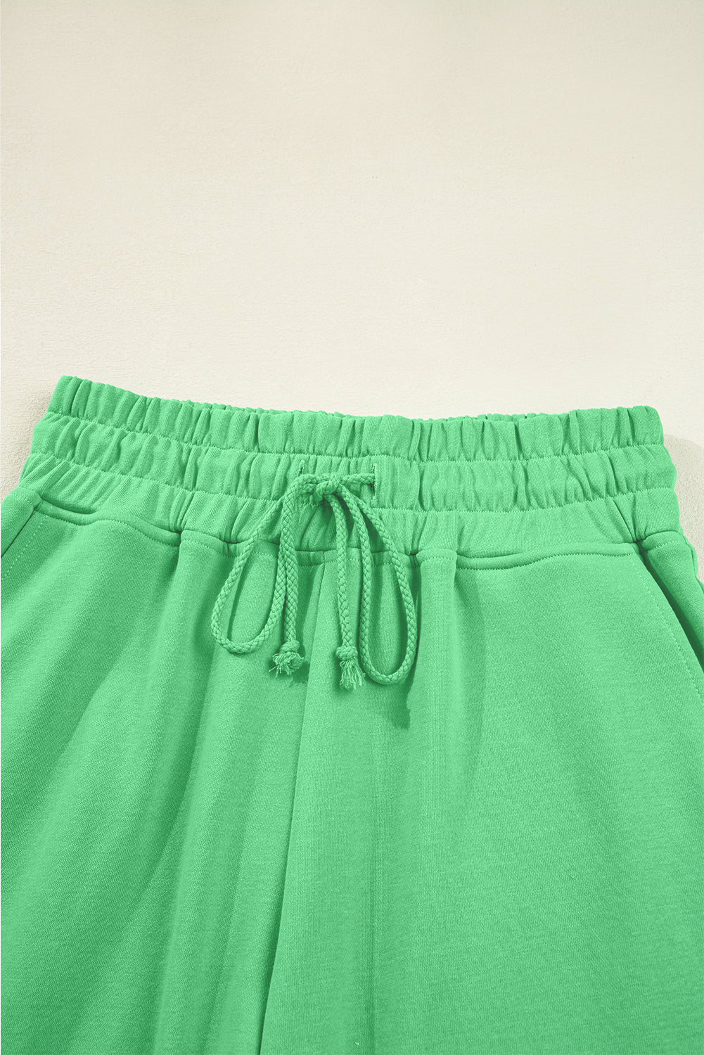 Green sweatpants with drawstring on a light beige background