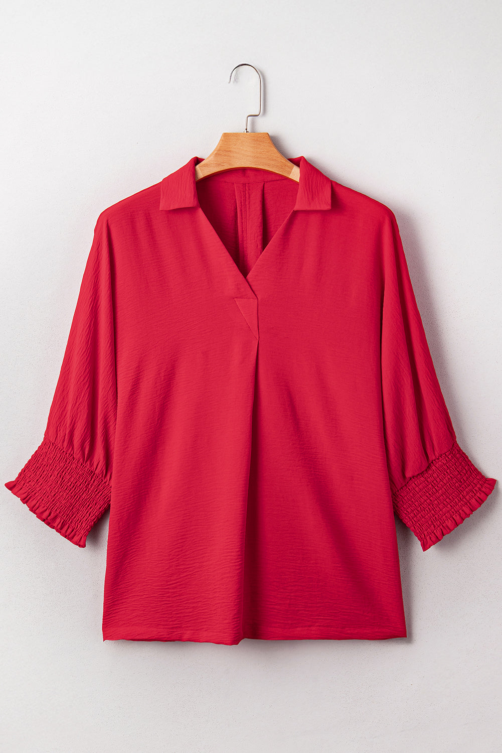 Red blouse with smocked cuffs on a wooden hanger against a white background