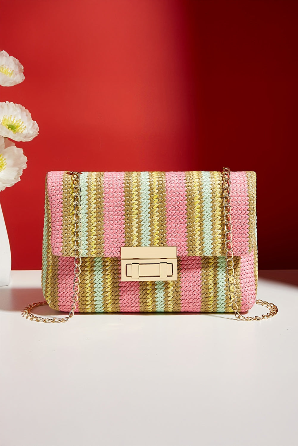 Striped handbag with a gold chain on a white surface against a red background front view