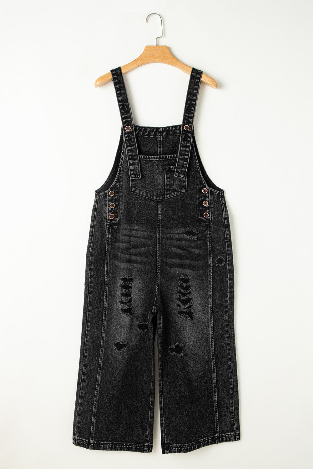 Black denim overalls on a hanger against a white background