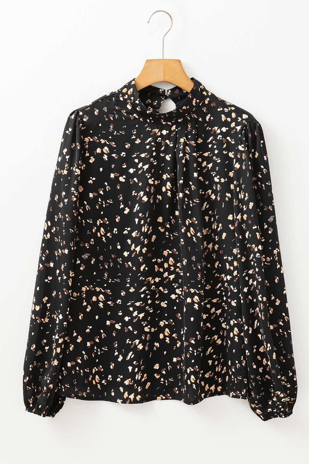 Black blouse with beige pattern on a wooden hanger against a white background