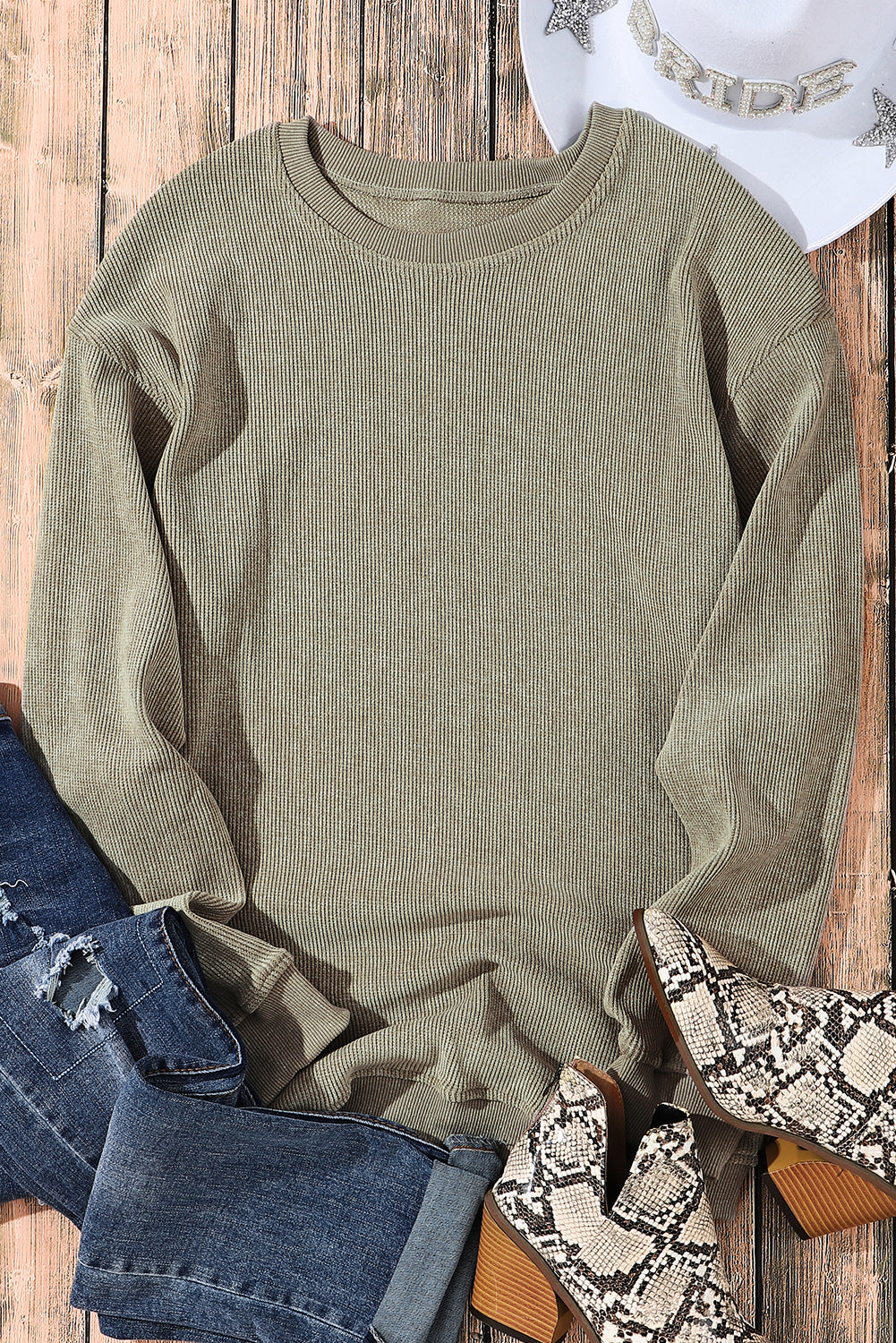 Green ribbed sweater with denim jeans and patterned shoes on a wooden surface