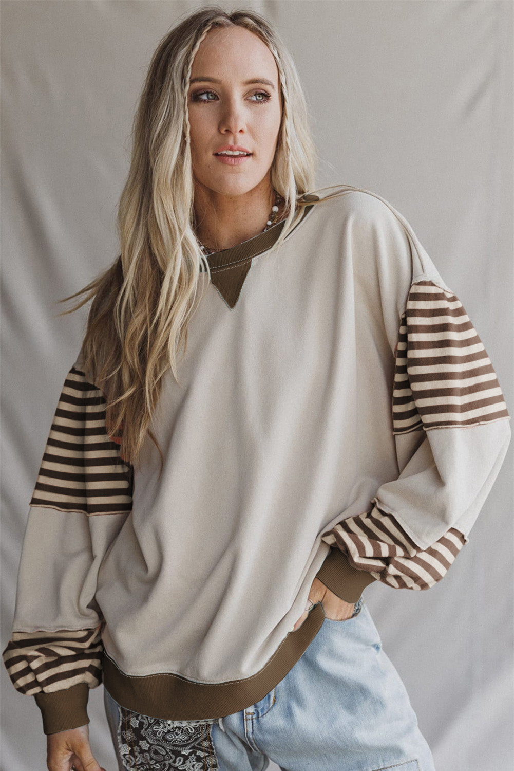Woman wearing a beige sweater with striped sleeves against a plain background