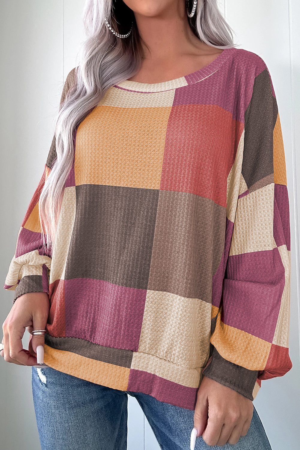 Person wearing a colorful patchwork sweater with a neutral background