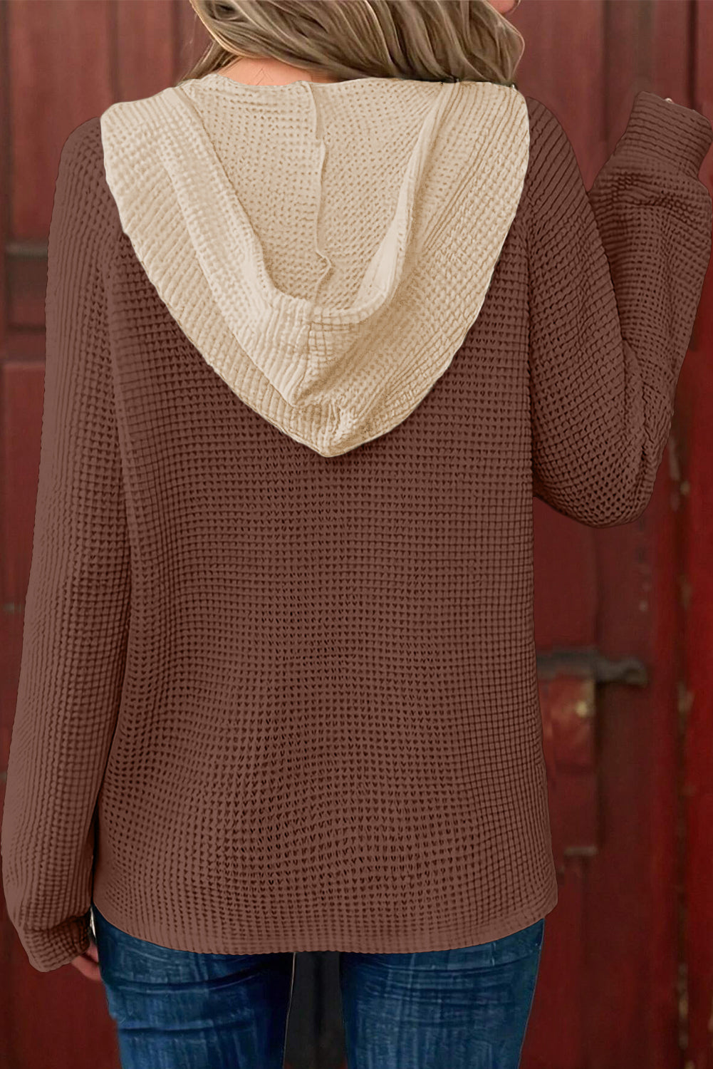 Brown textured hoodie with beige hood worn by a person, standing against a red background.