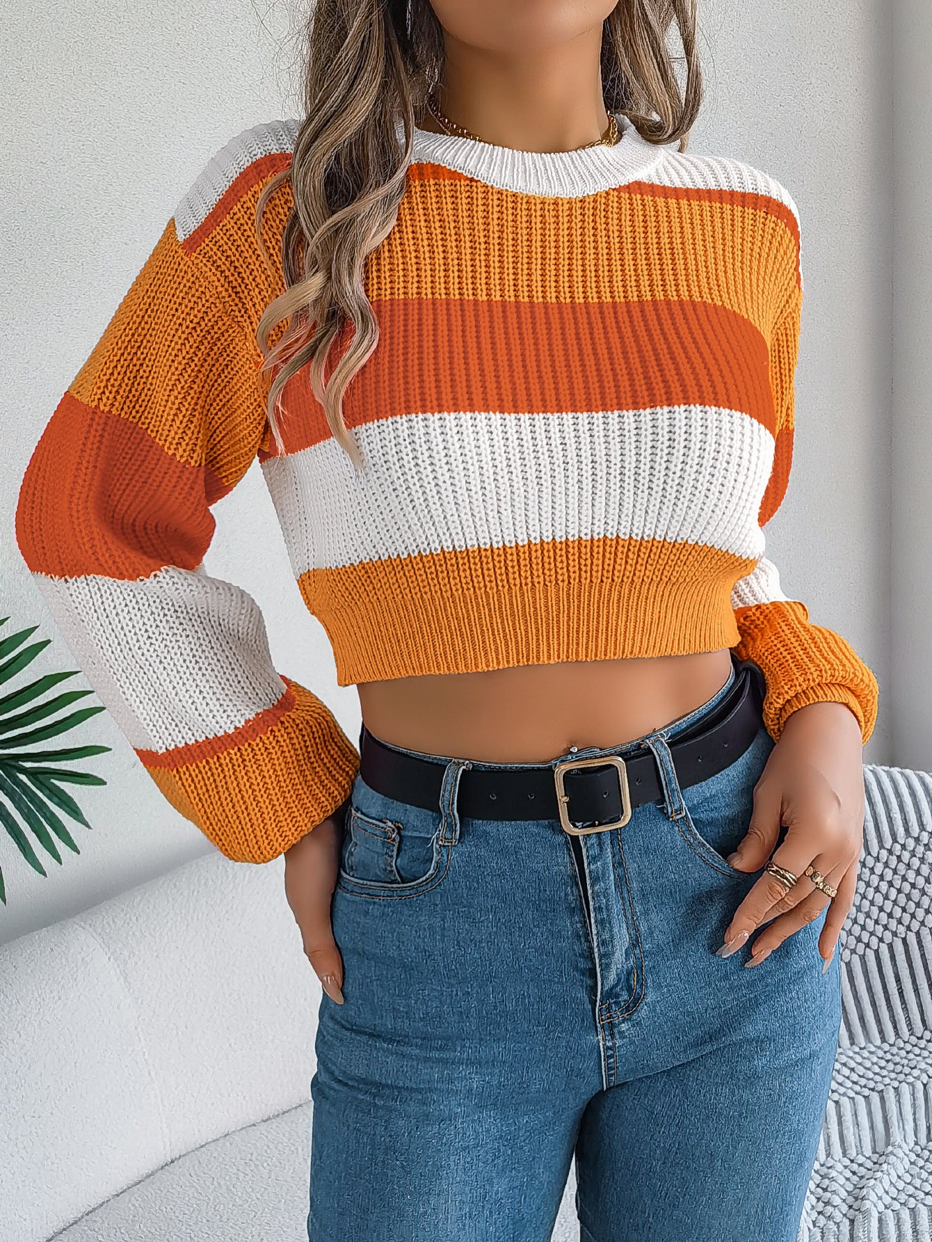 Person wearing a striped orange and white sweater with blue jeans indoors.