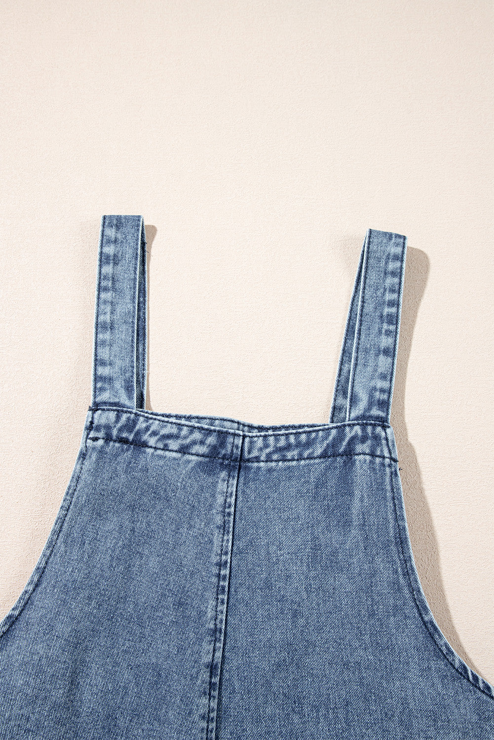 Blue denim pinafore dress on a beige background