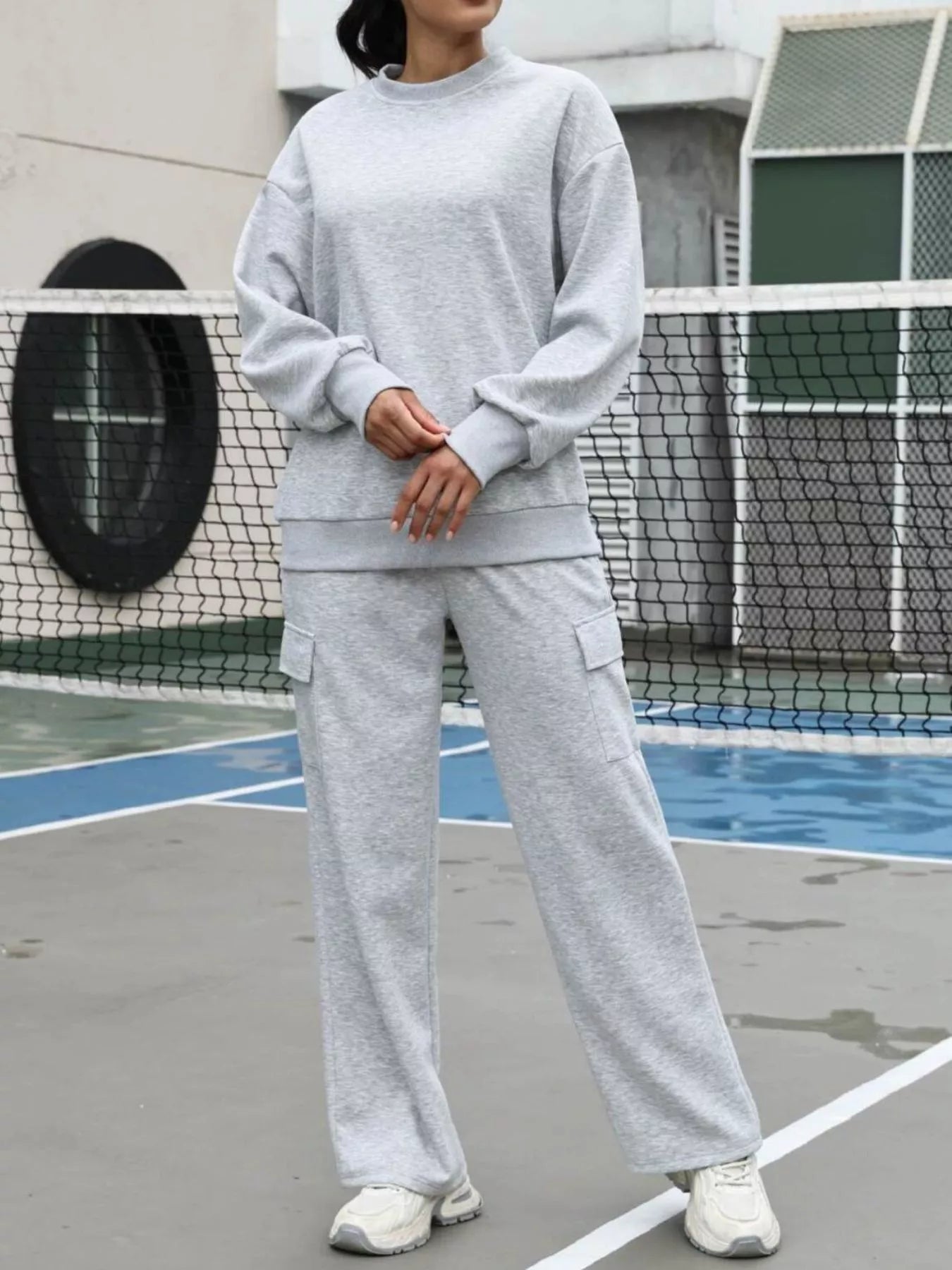 Person wearing a gray sweatshirt and pants on a tennis court