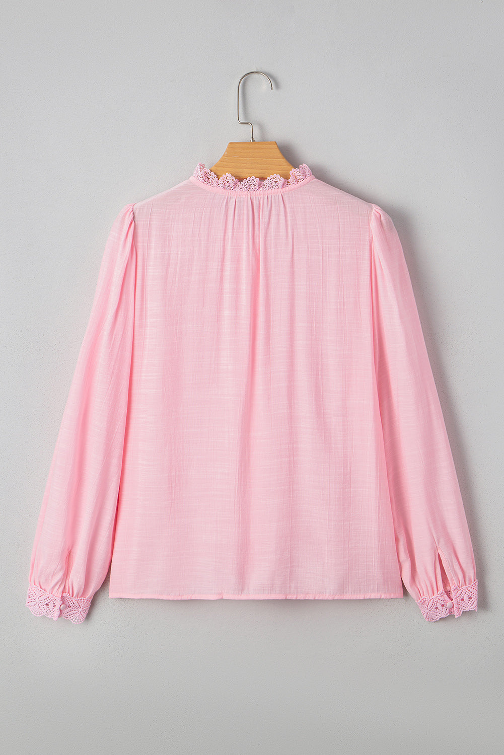 Pink blouse with lace details on a hanger against a gray background