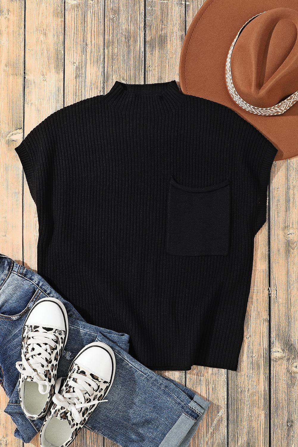 Black sleeveless top with a pocket, blue jeans, white sneakers, and a brown hat on a wooden surface.