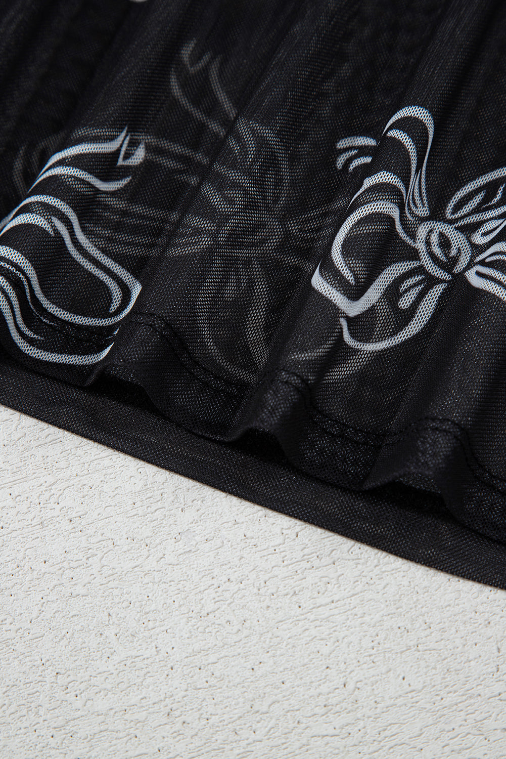 Black tulle fabric with white floral patterns on a textured surface