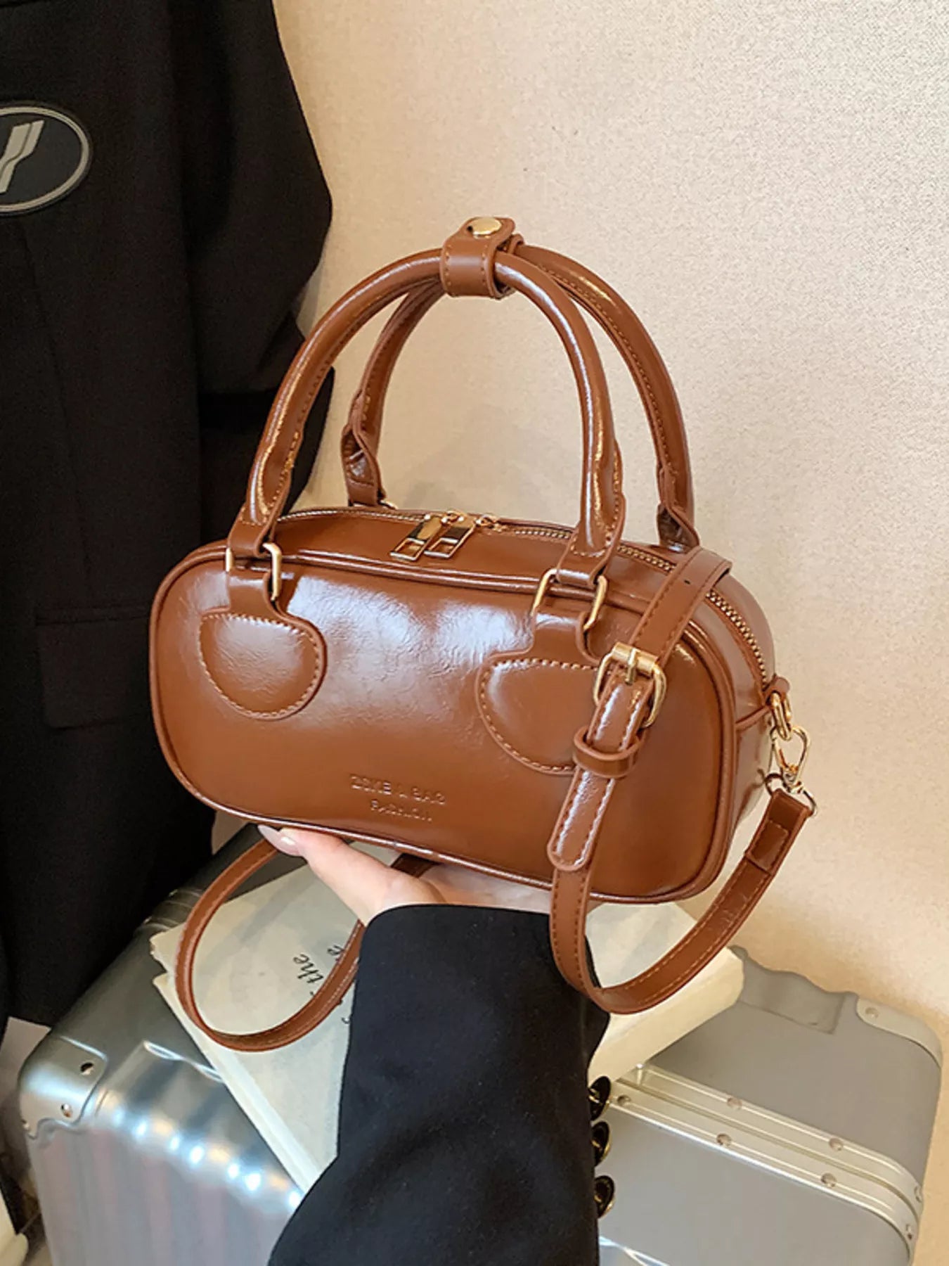 Brown handbag held by a person with suitcases in the background
