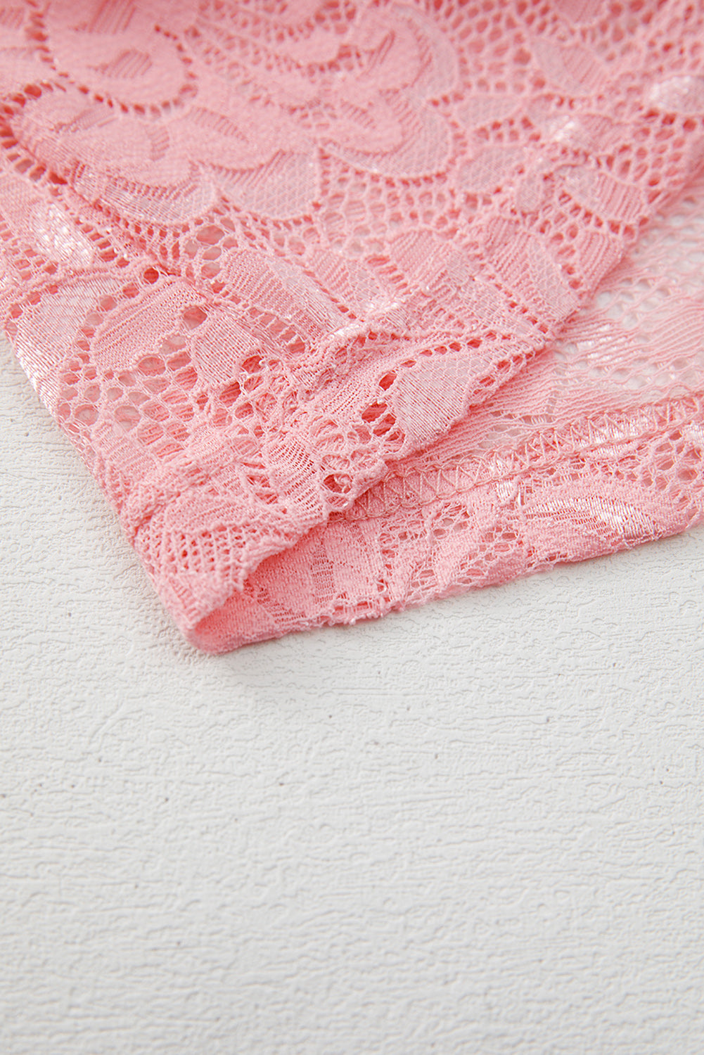 Close-up of pink lace fabric on a textured white background
