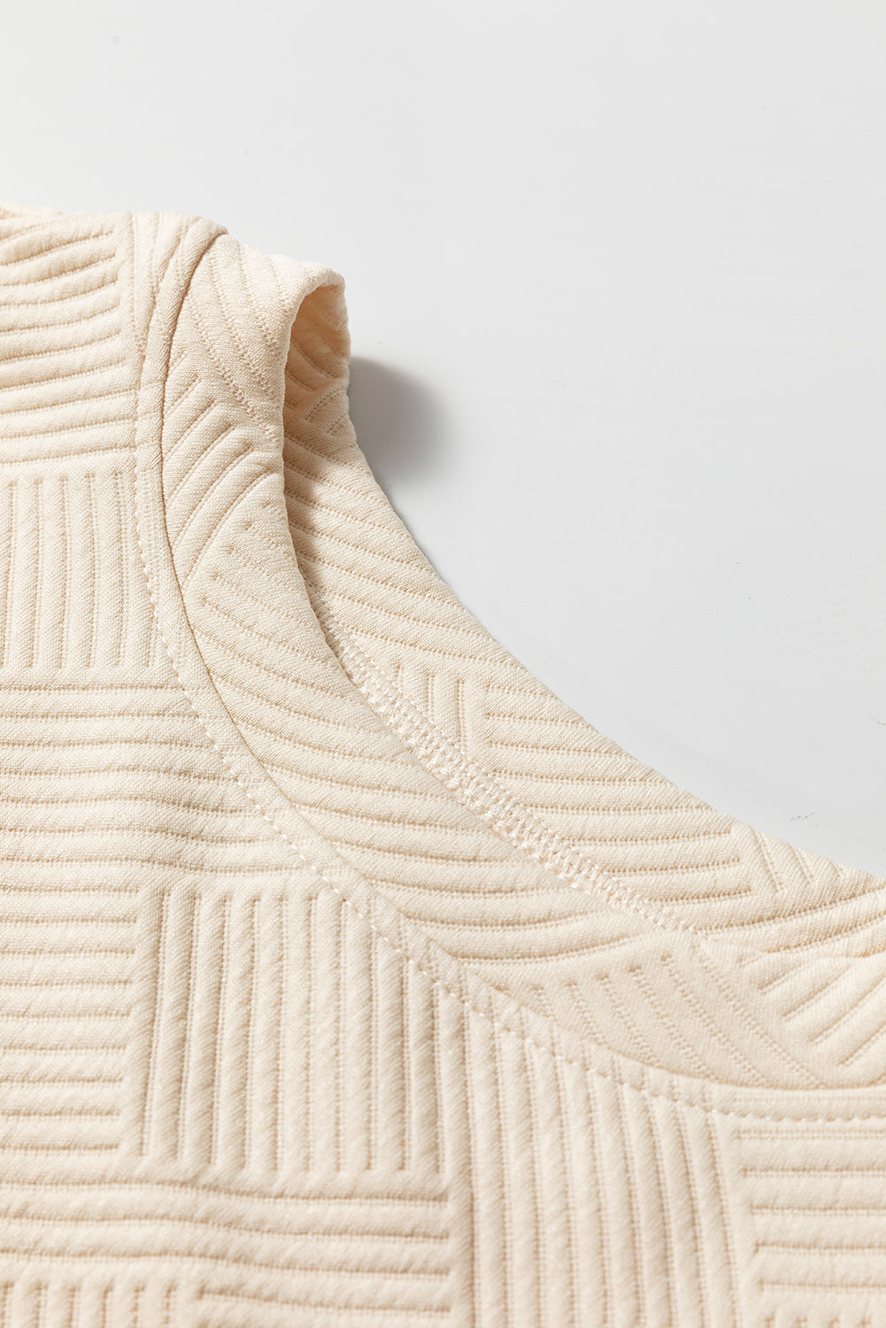 Close-up of a textured beige fabric with a subtle pattern on a light gray background