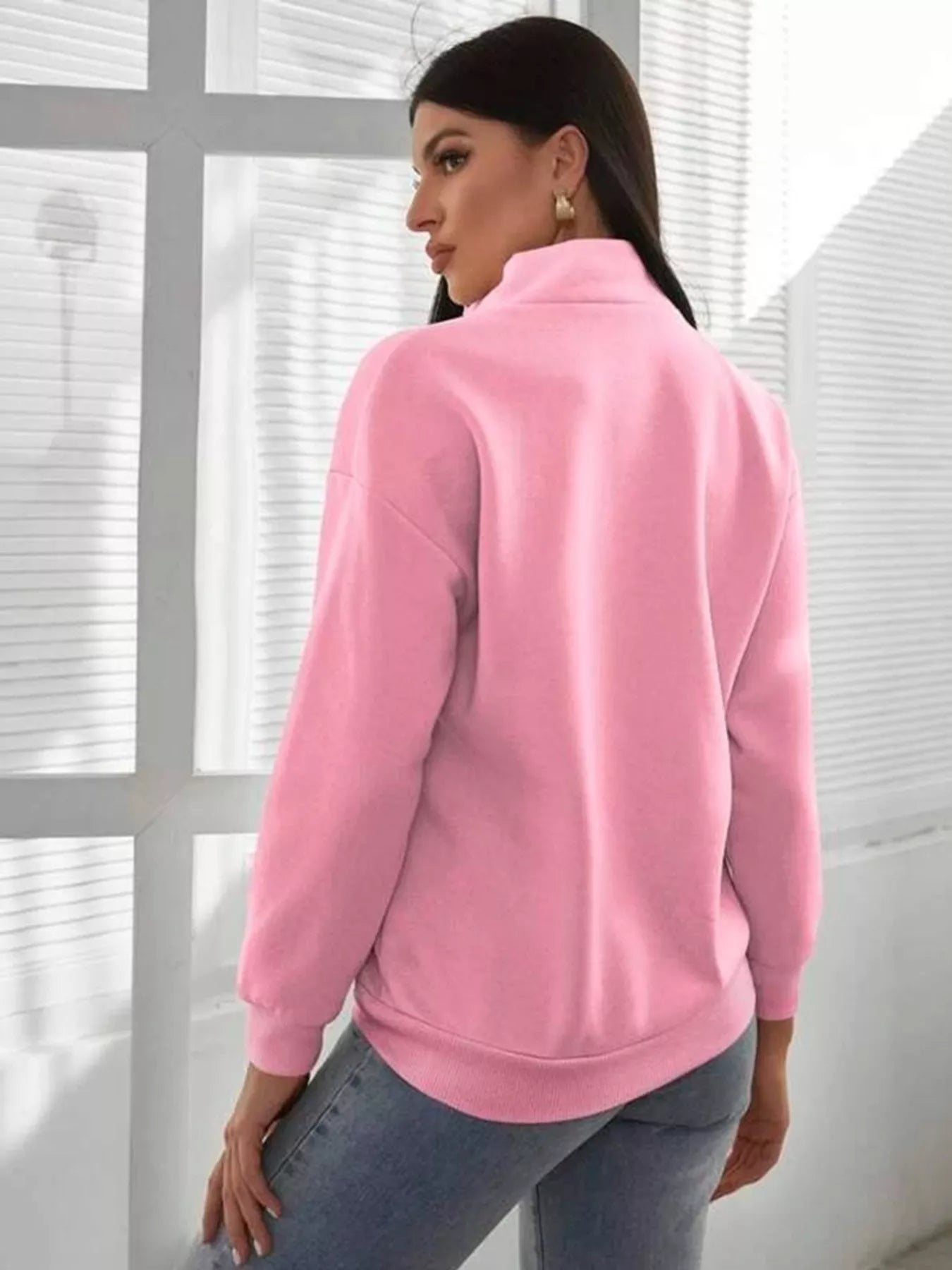 Woman wearing a pink jacket in front of a window with blinds
