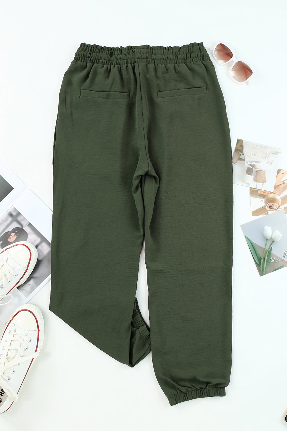 Green pants on a white background with scattered items. Back view