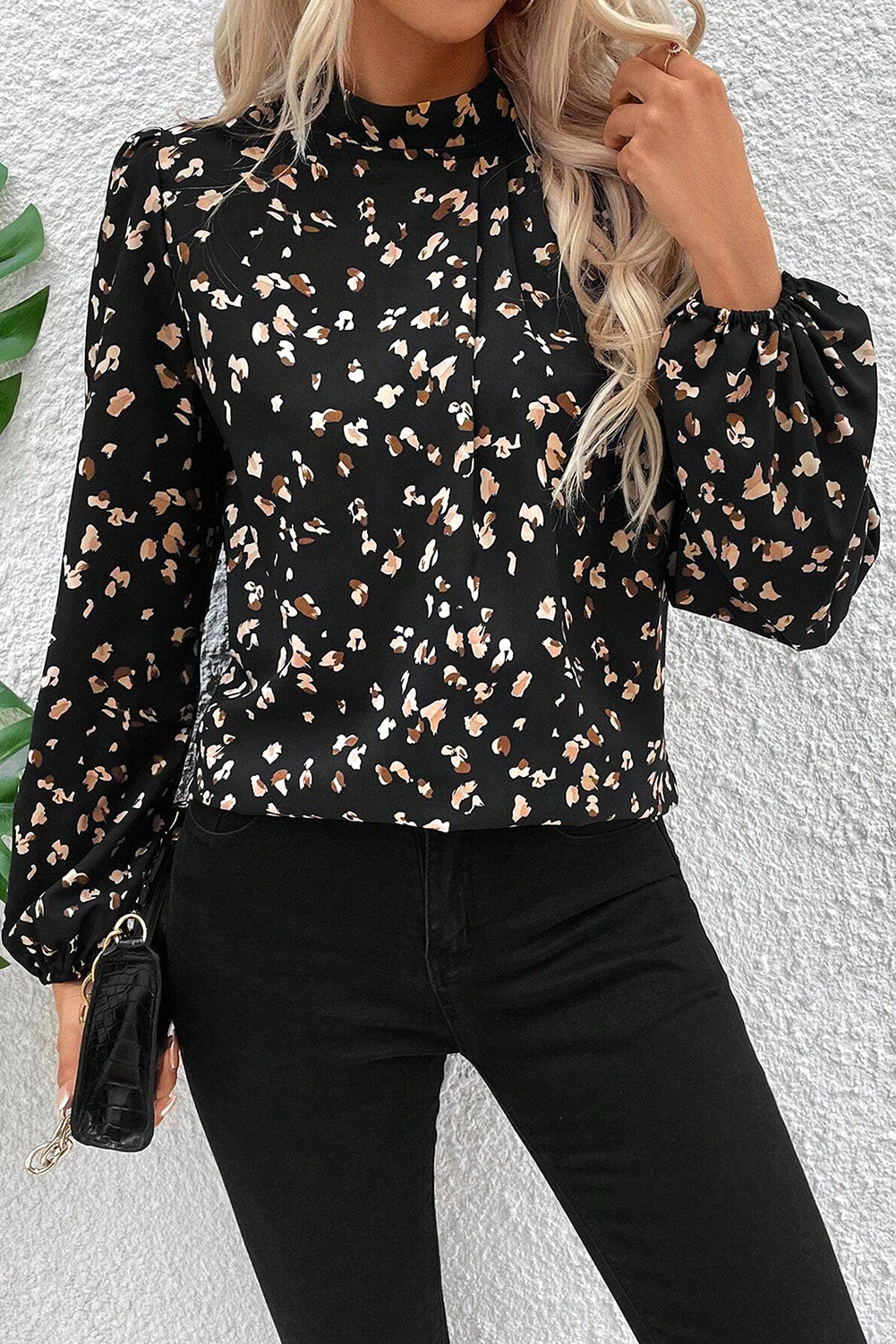 Person wearing a black floral blouse with long sleeves against a white wall.