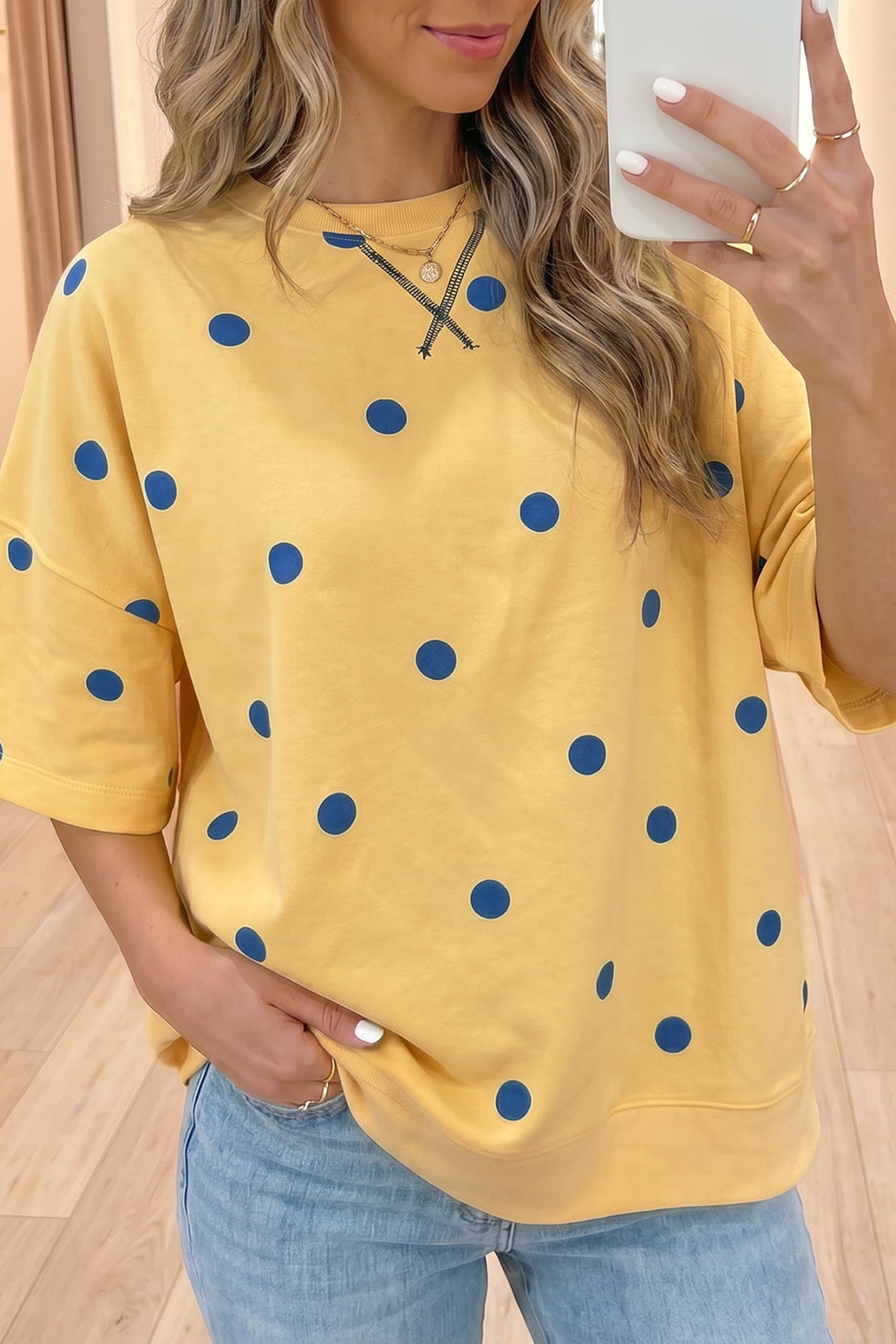 Person wearing a yellow shirt with blue polka dots and light blue jeans indoors.