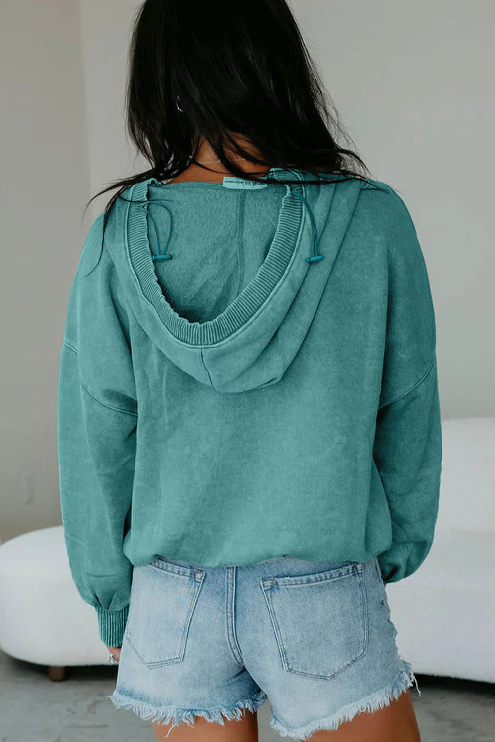 Person wearing a teal hoodie and denim shorts against a neutral background