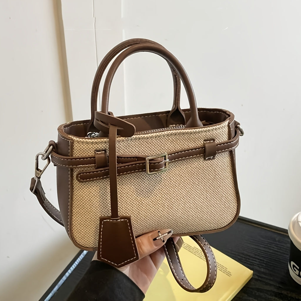 Brown handbag with beige accents held by a person against a neutral background