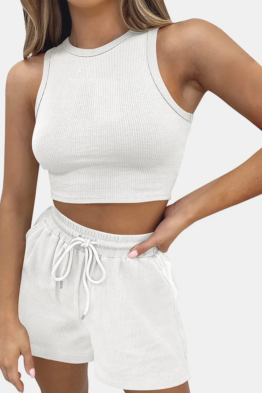 Woman wearing a white ribbed tank top and shorts on a plain background