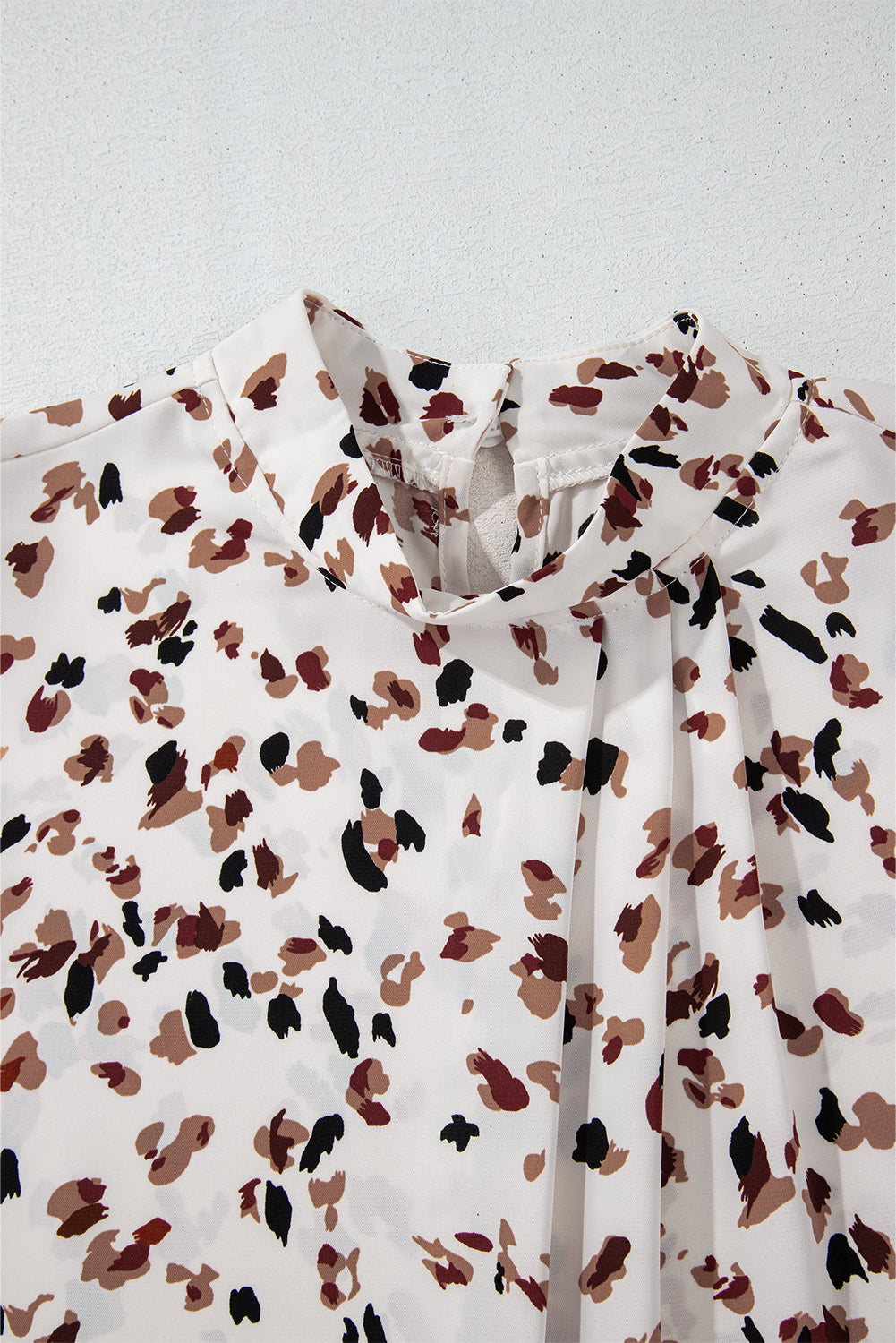 White blouse with brown and black abstract pattern on a light gray background