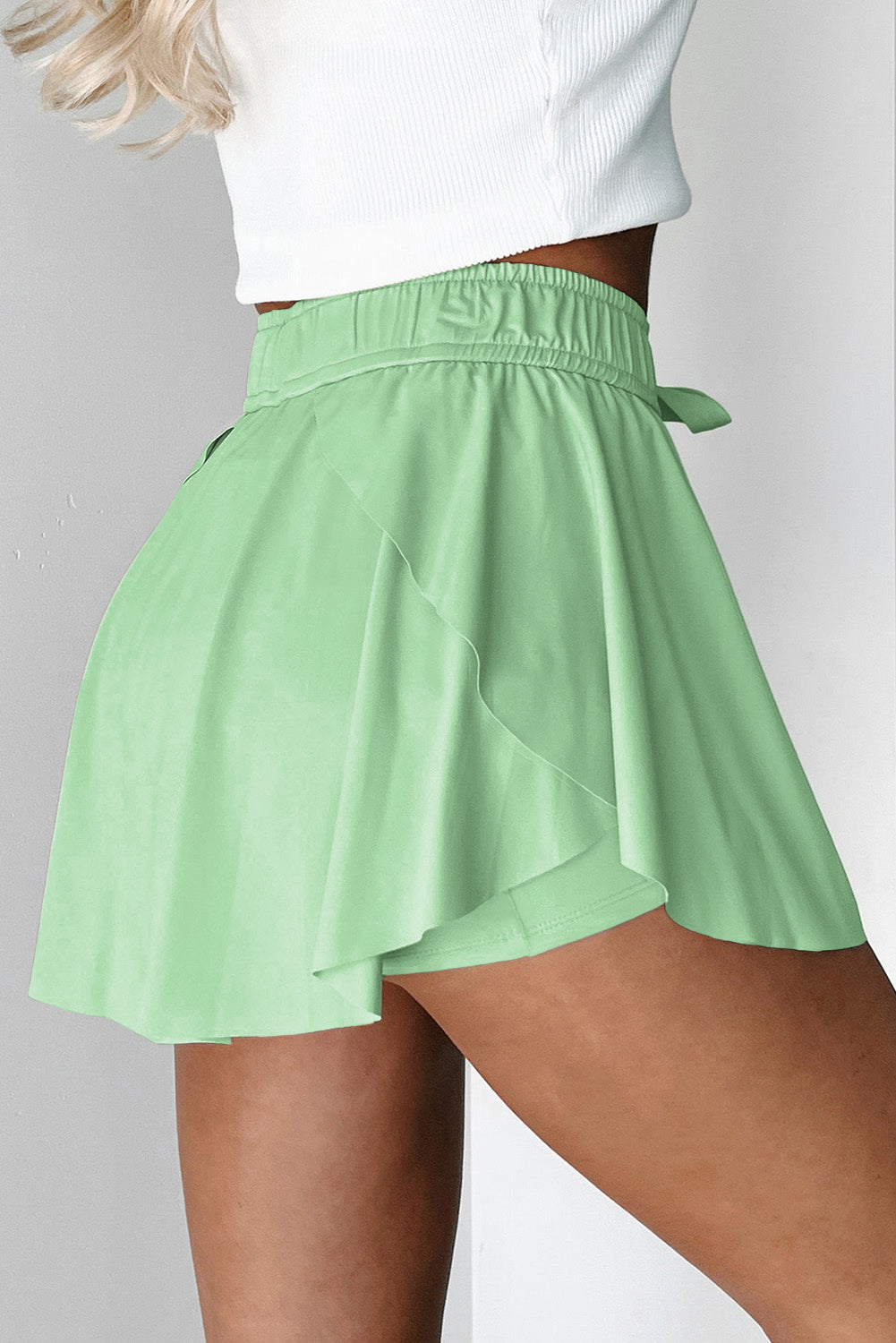 Green tenni shorts worn by a person on a plain background side view 