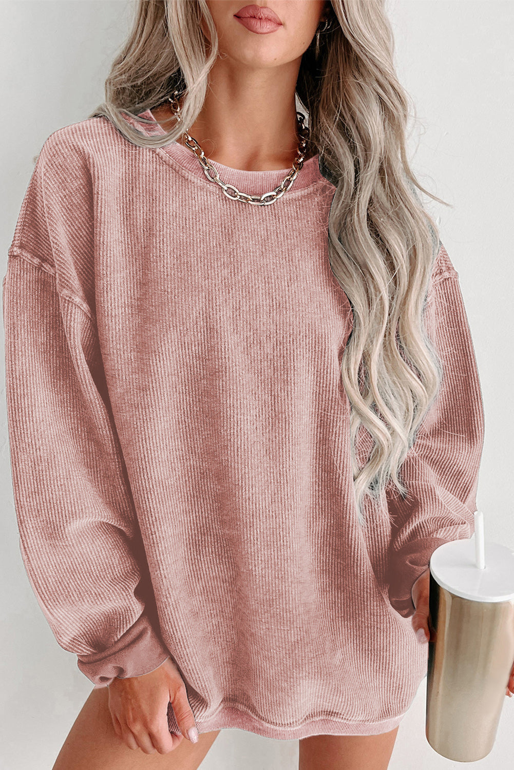 Person wearing a pink corduroy dress holding a white cup with a straw on a light background