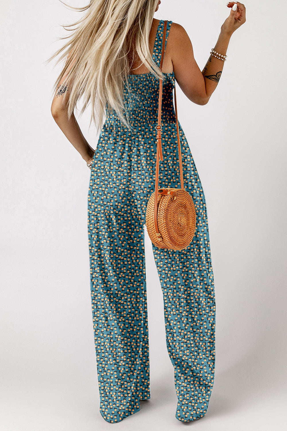 Woman wearing a blue floral jumpsuit holding a round woven bag on a white background