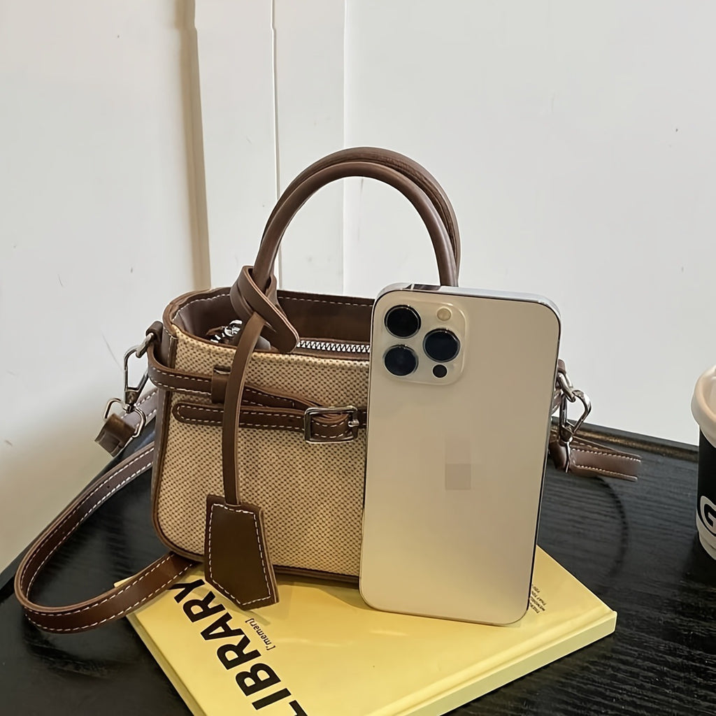 Beige handbag with brown strap, smartphone, and book on a table
