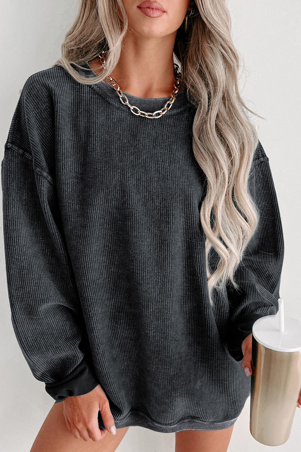 Woman wearing a dark gray oversized sweater holding a metallic cup against a white background