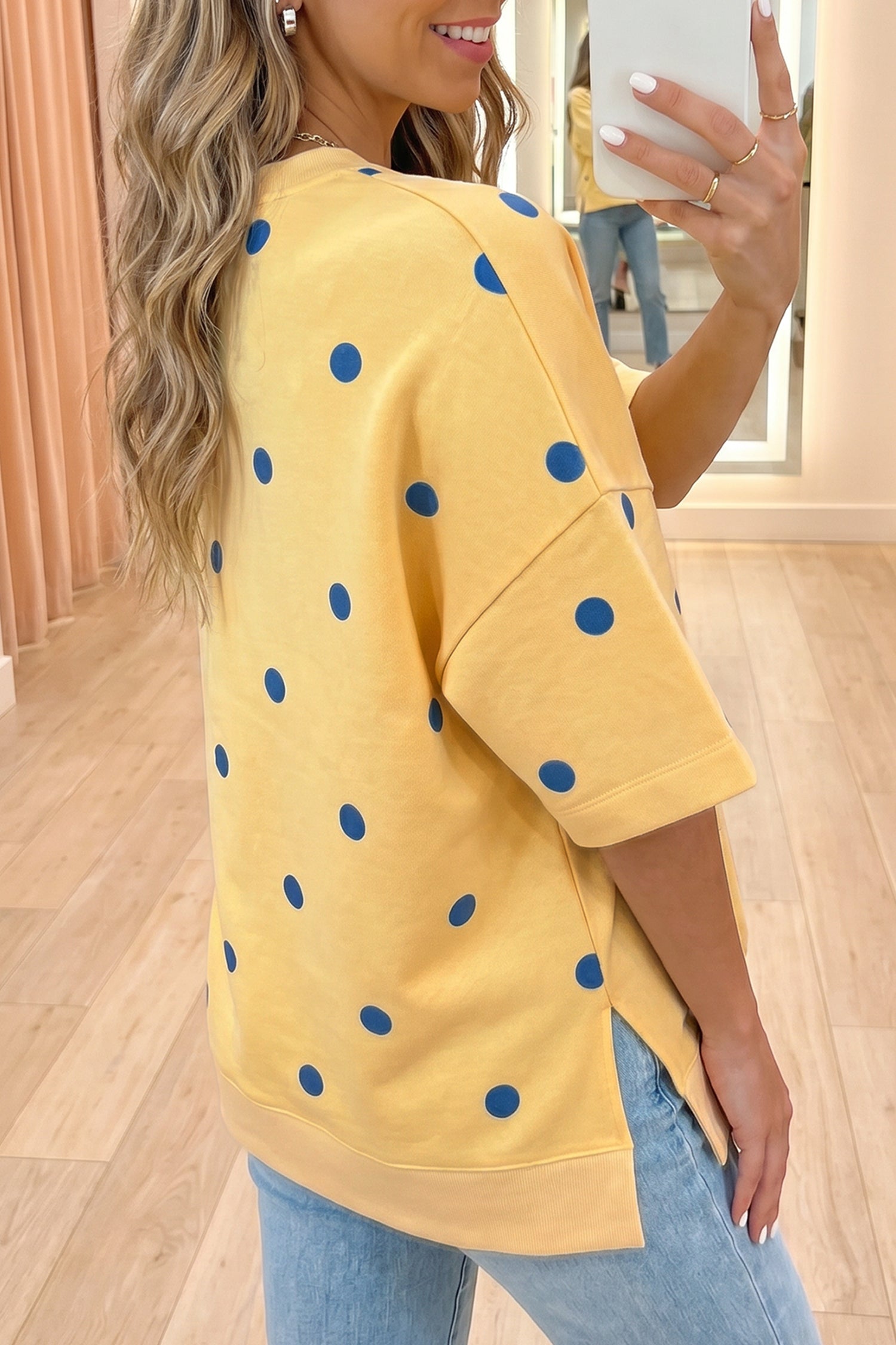 Person wearing a yellow sweater with blue polka dots, taking a mirror selfie. Angle view