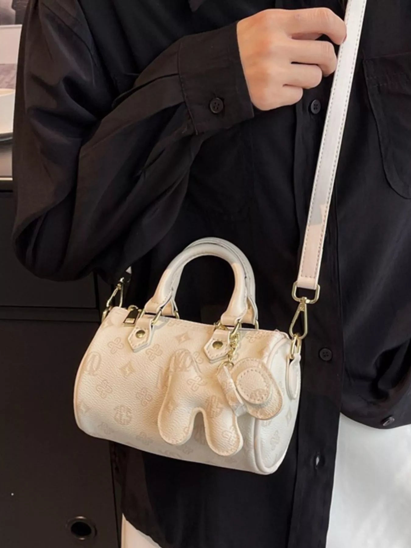 Person holding a beige handbag with gold accents against a black background