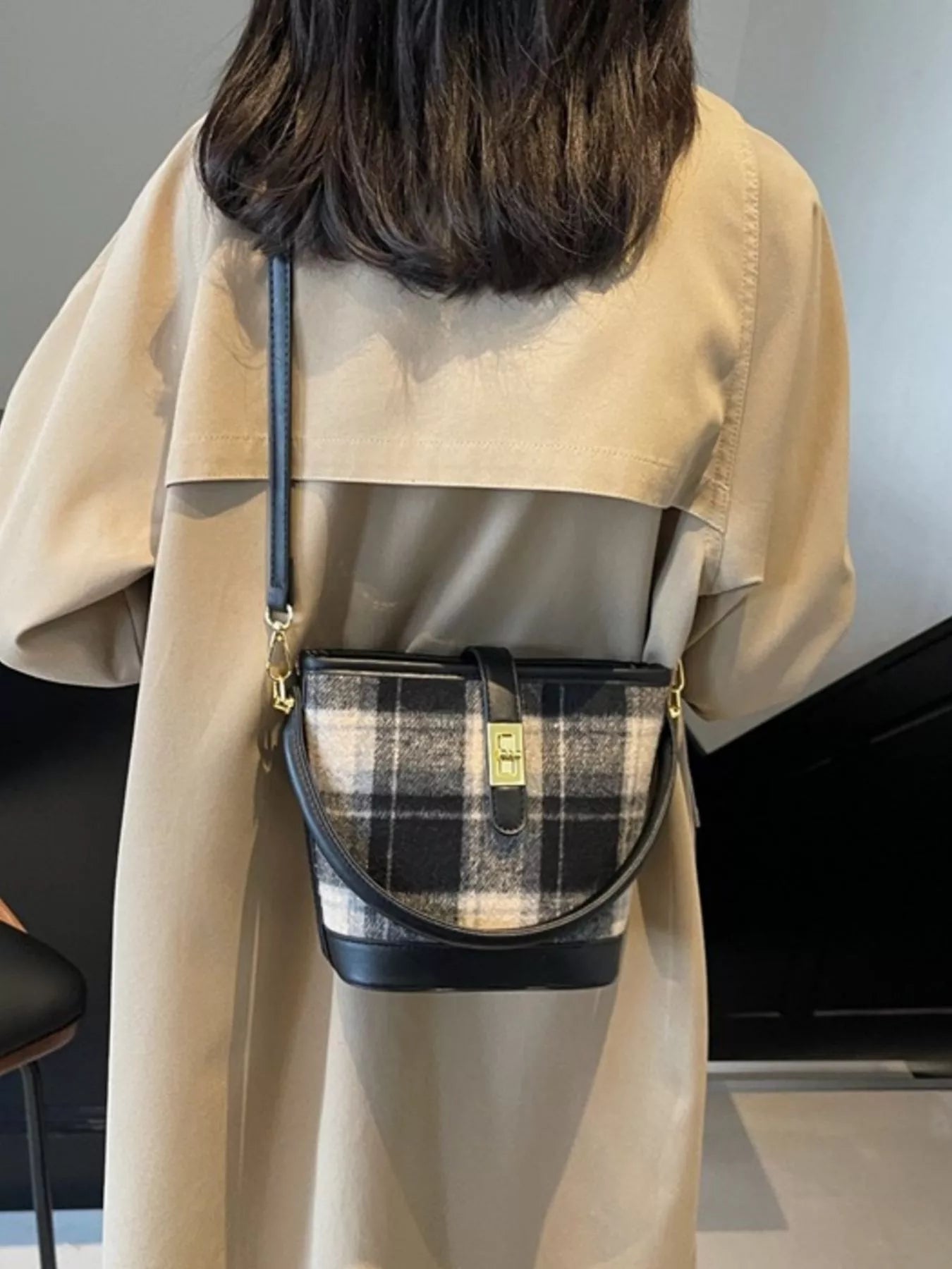 Person wearing a beige trench coat with a plaid handbag over one shoulder.