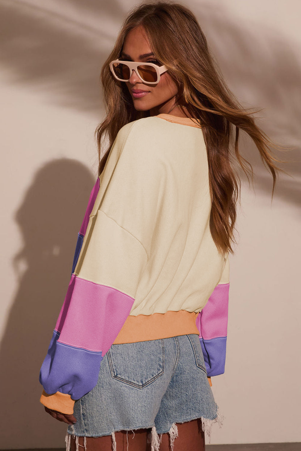 Woman wearing a colorful sweater and sunglasses against a neutral background