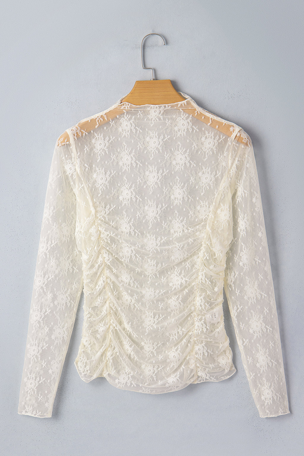 White lace blouse on a hanger against a gray background