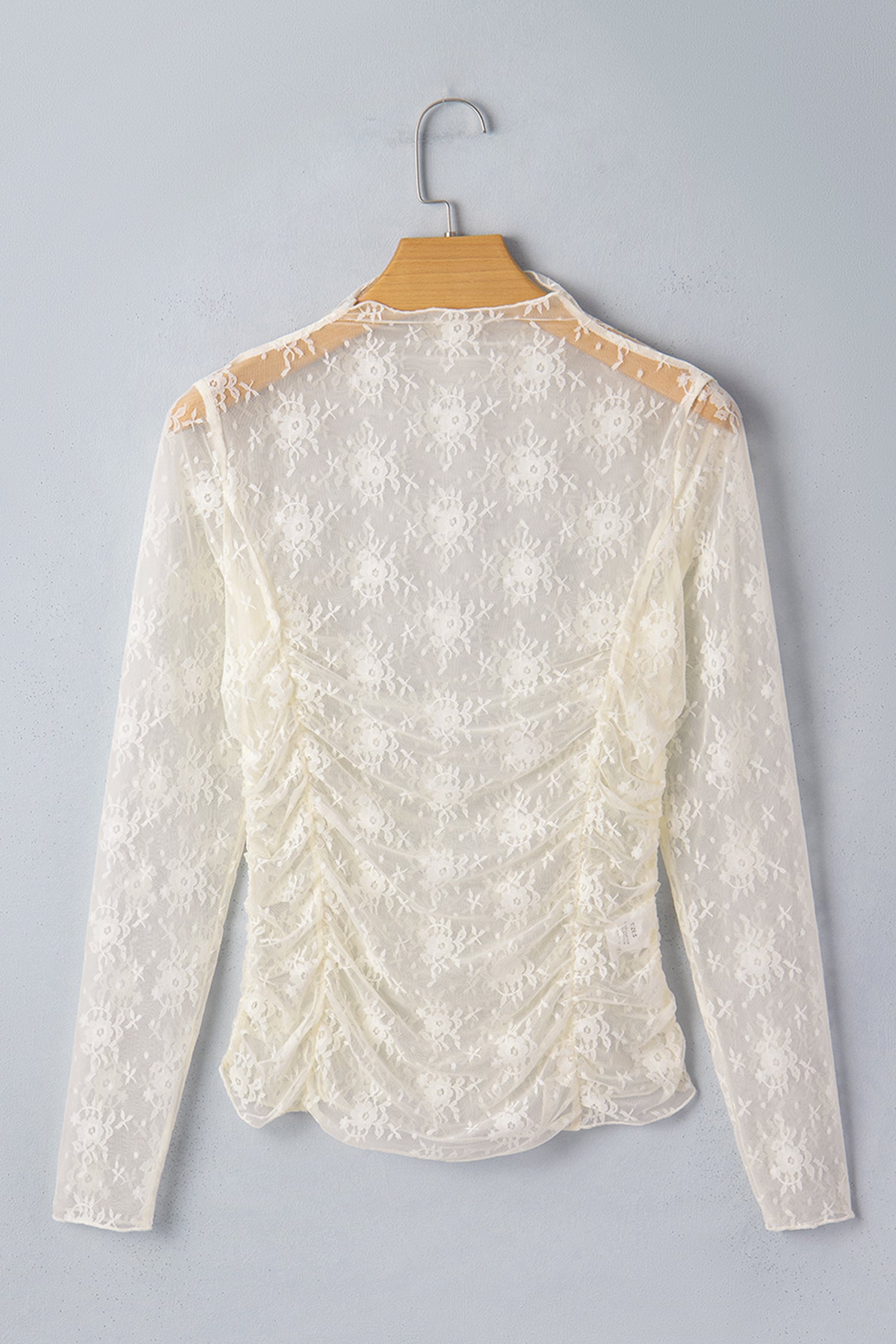 White lace blouse on a hanger against a gray background