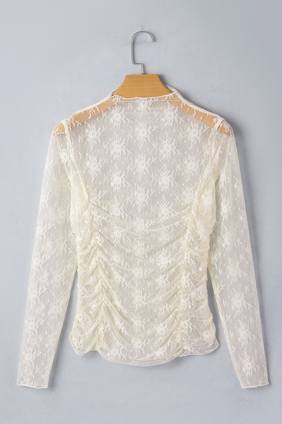 White lace blouse on a hanger against a gray background