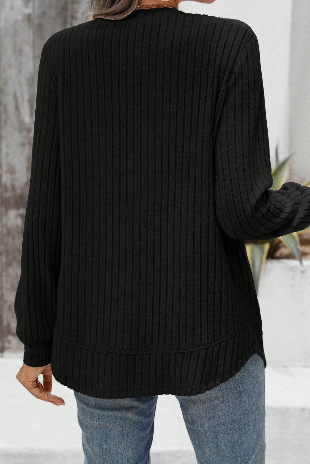 Person wearing a black ribbed sweater with a blurred background