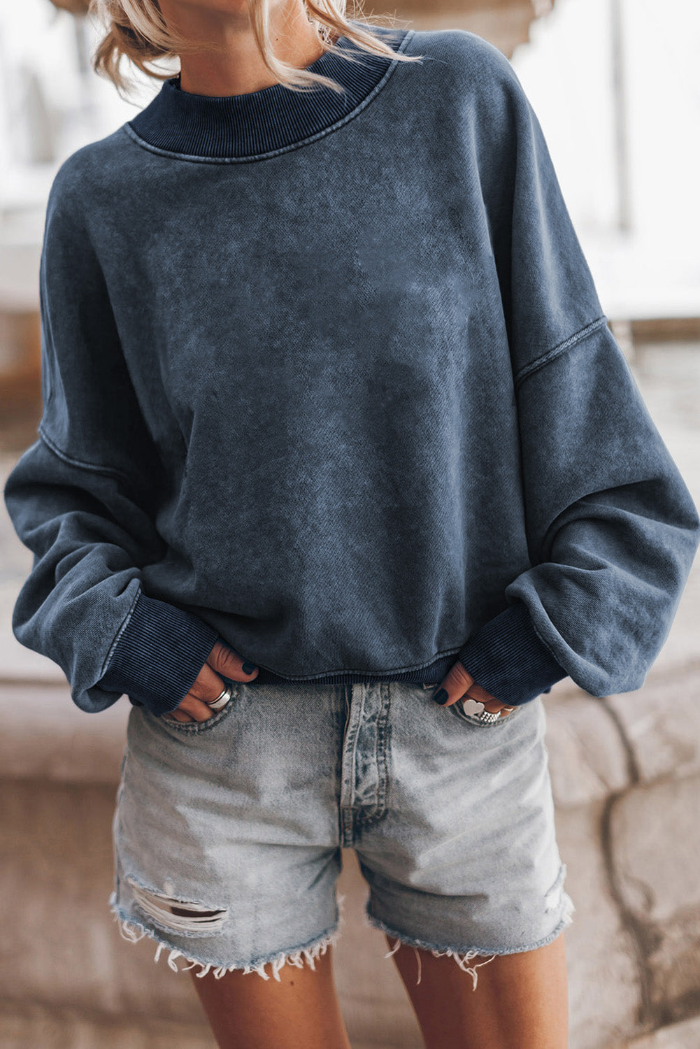 Person wearing a blue sweatshirt and denim shorts indoors