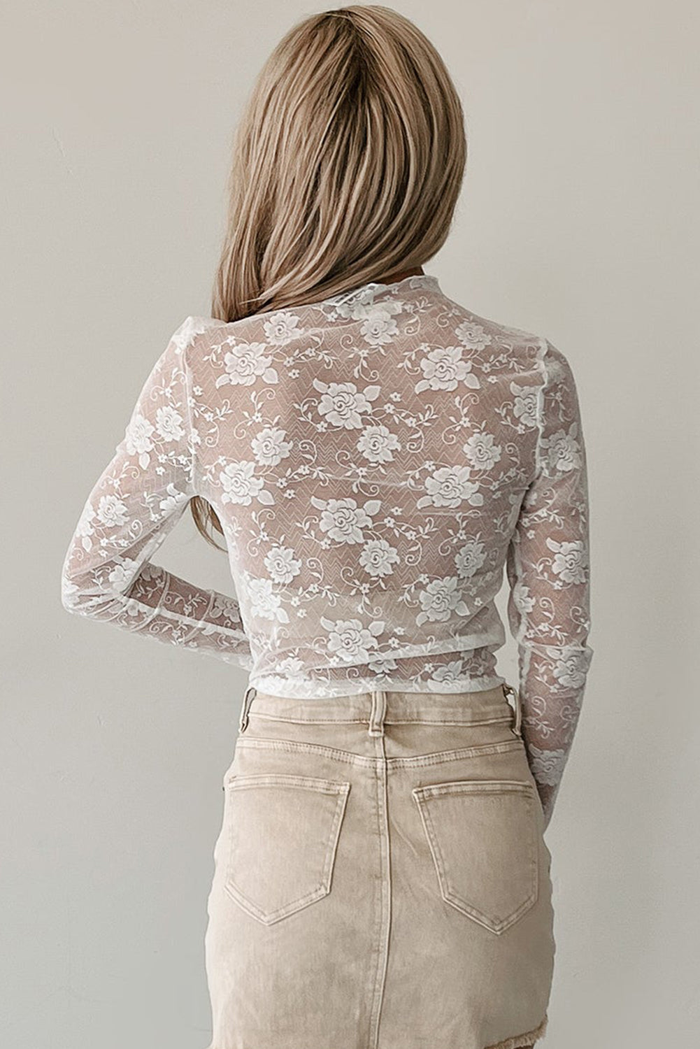 Person wearing a floral lace top and beige pants against a plain background
