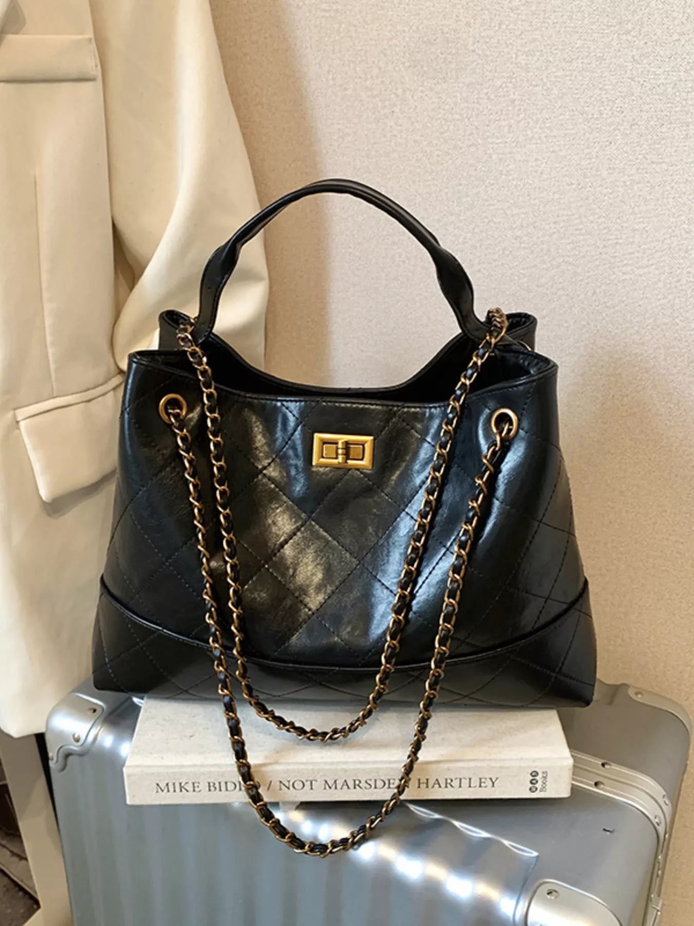 Black handbag with gold chain on a suitcase and books