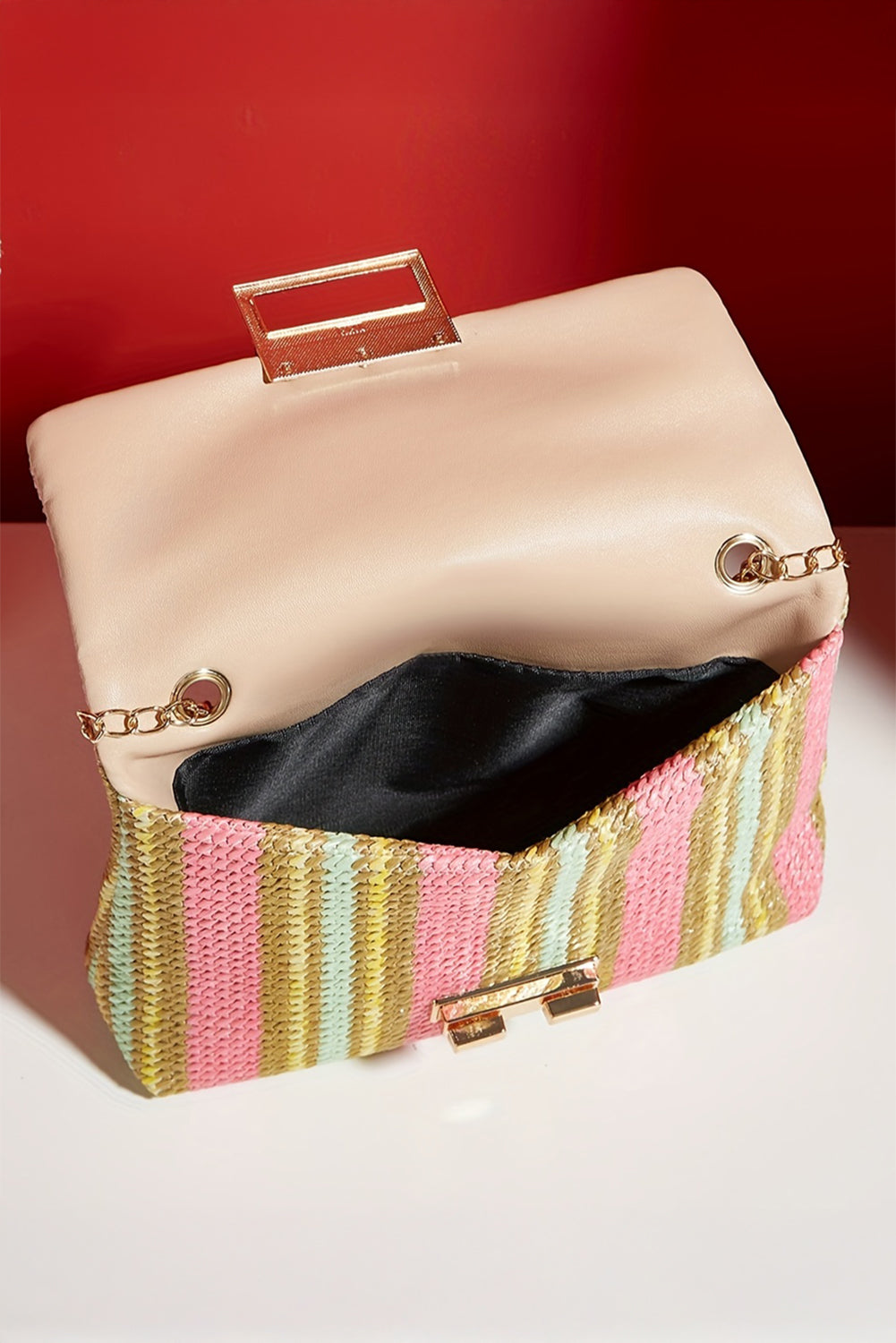 Clutch bag with a striped pink and gold base on a white surface with a red background open view