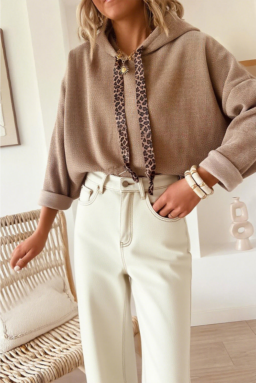 Person wearing a beige hoodie with a leopard print drawstring and white pants in an indoor setting.