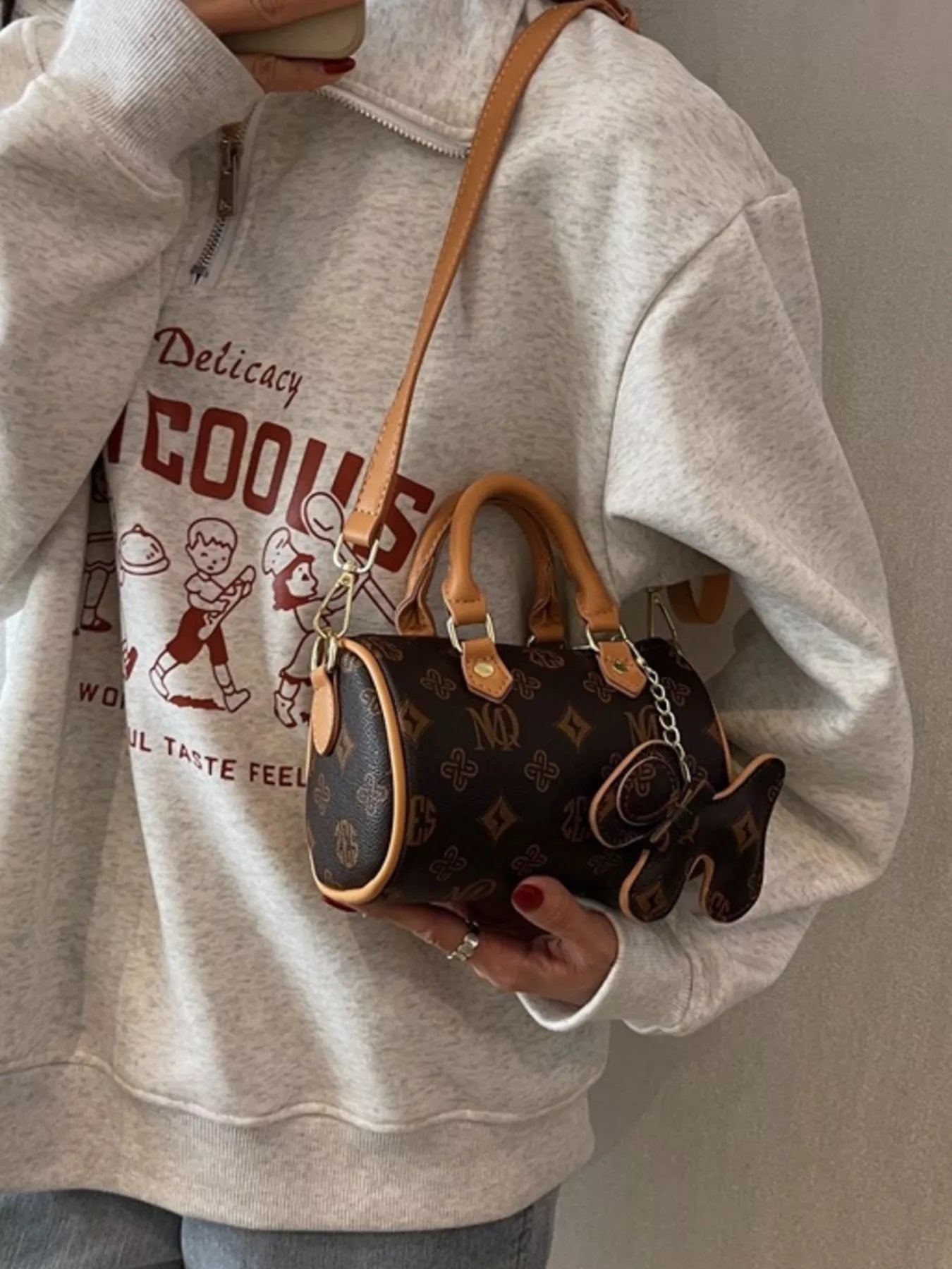 Person wearing a gray hoodie with graphic design, holding a brown handbag.