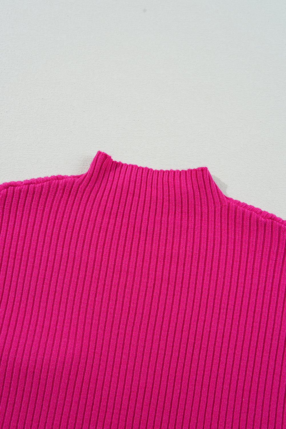 Close-up of a bright pink ribbed sweater on a light gray background