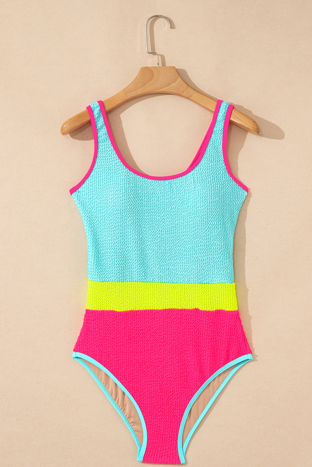 Colorful swimsuit with pink, green, and blue sections on a beige background