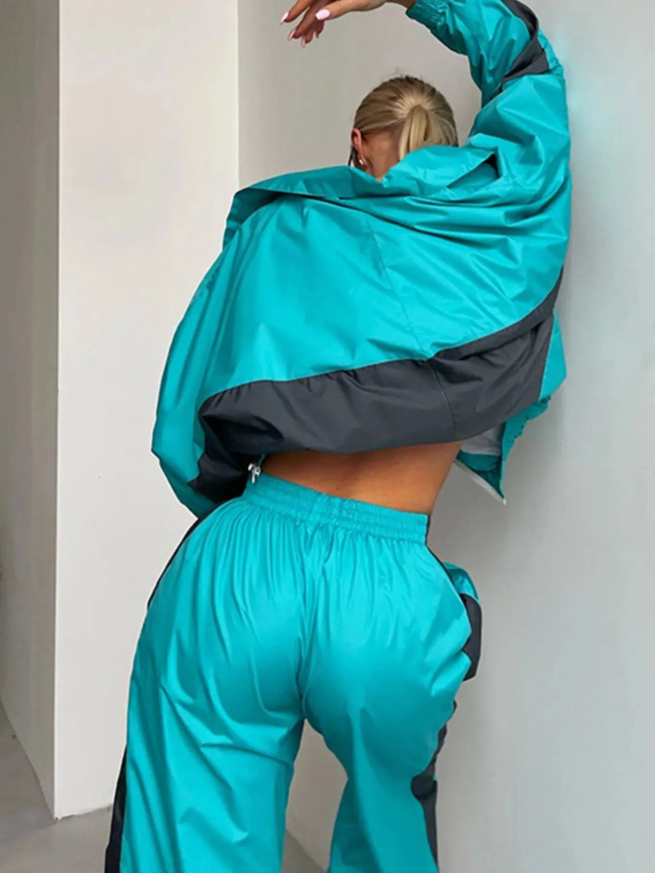 Person wearing a teal and black tracksuit against a white wall