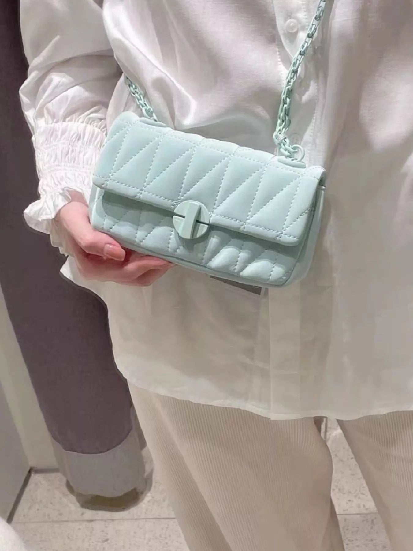 Person holding a light blue quilted handbag with a chain strap.