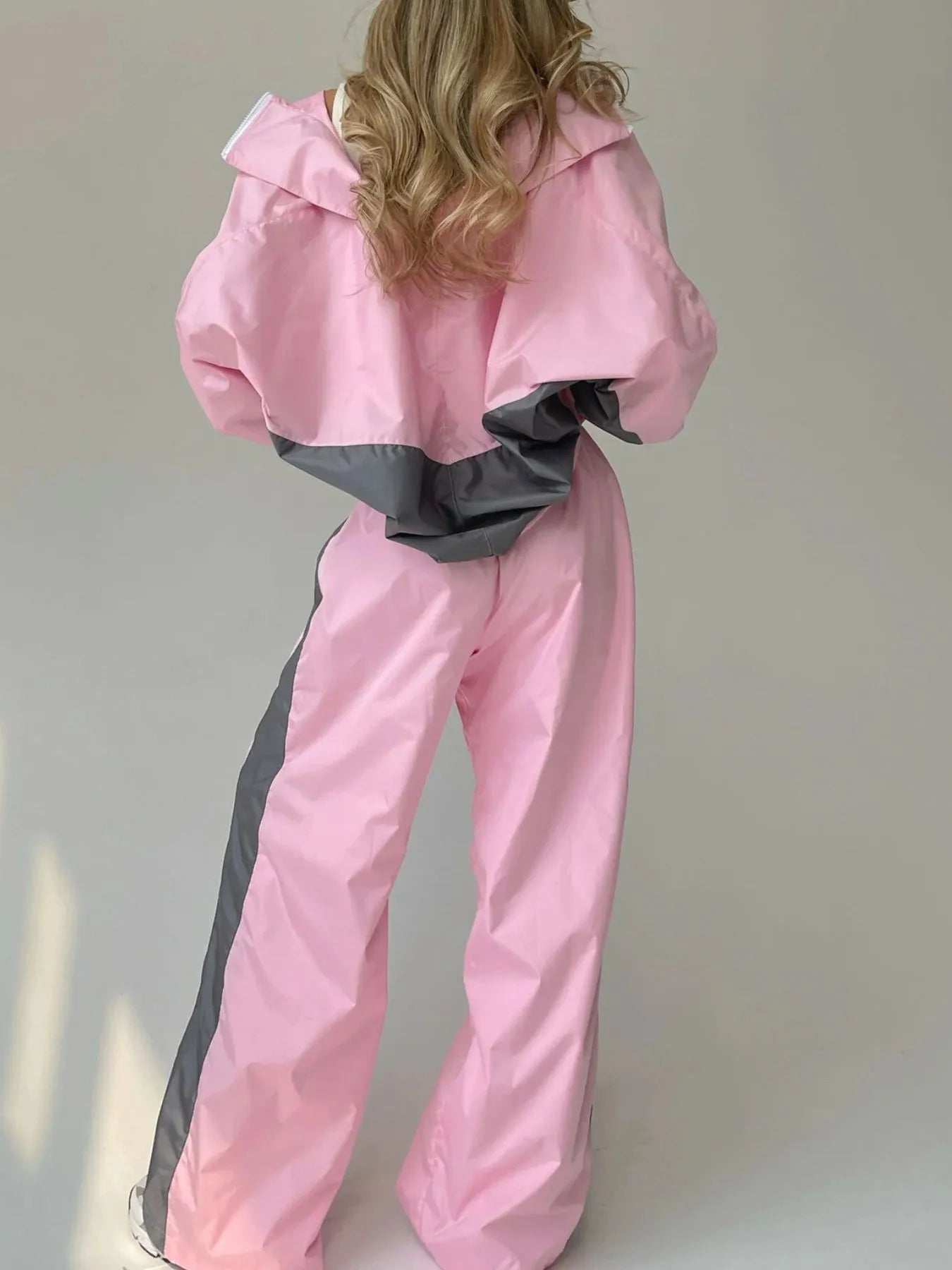 Person wearing a pink and gray outfit with a hood against a plain background